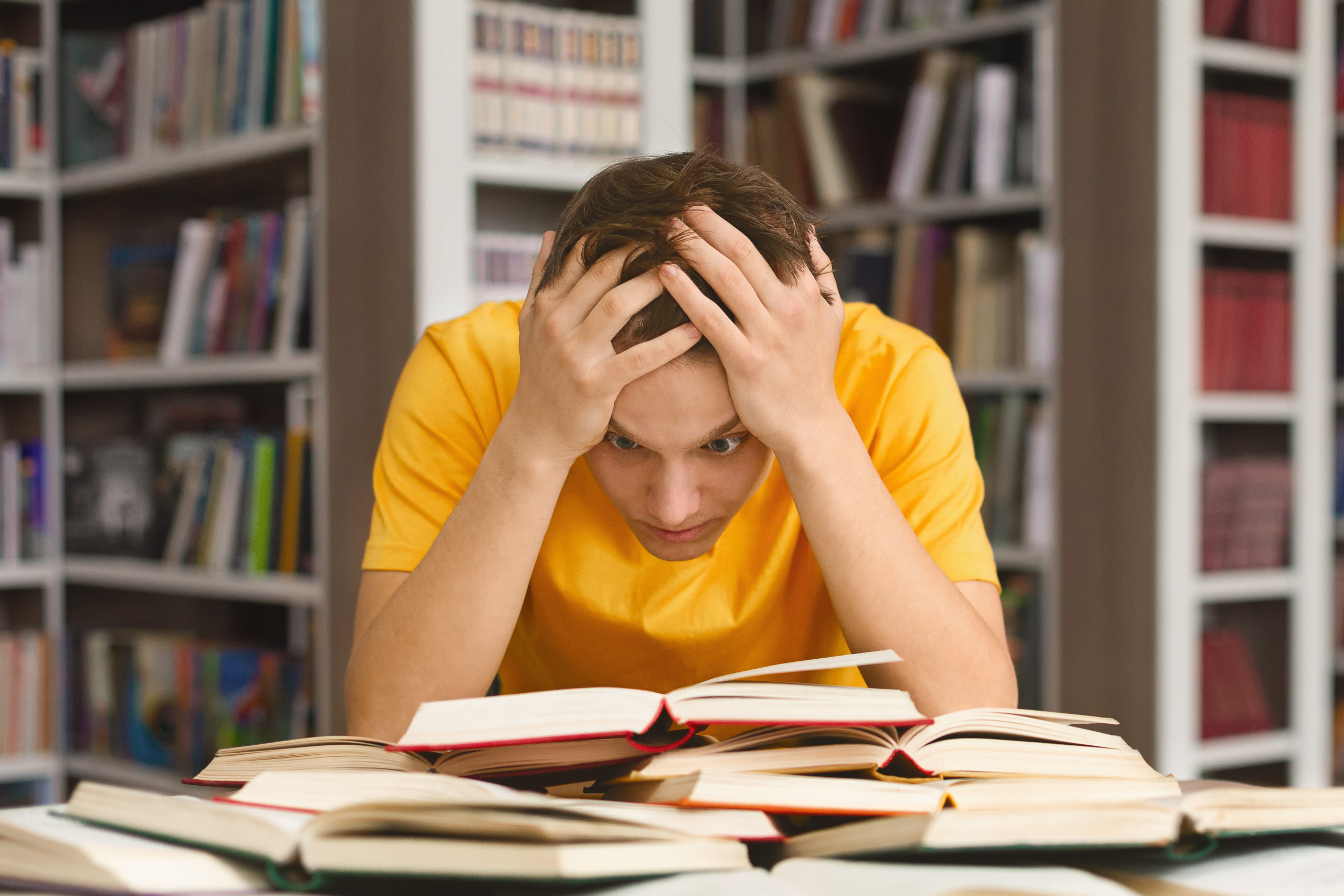 Exhausted guy holding his head and reading book in library
